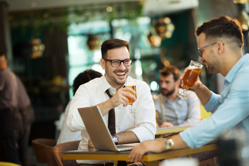 Two young businessmen use a laptop and drink beer
