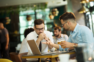 Two young businessmen use a laptop and drink beer