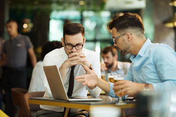 Two young businessmen use a laptop and drink beer