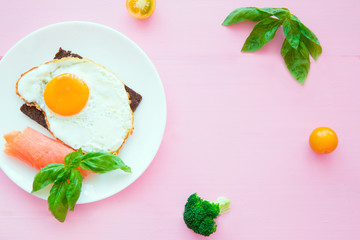 Fried eggs toasts with smoked salmon and broccoli on colorful pink table backgroud, copy space. 