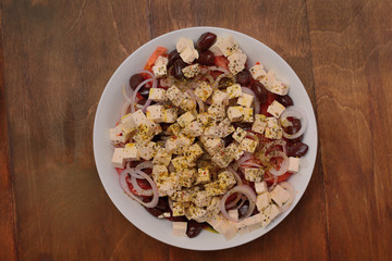 Greek salad in a large white plate on a wooden surface in the center. top view