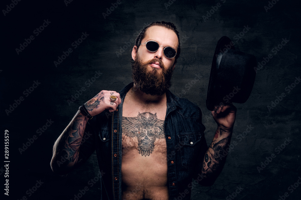 Wall mural Portrait of brutal man with open denim shirt and tattooed chest.