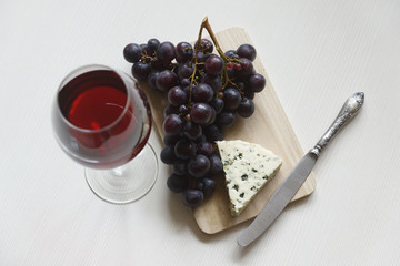 Red wine in an elegant glass, cheese and a bunch of grapes.