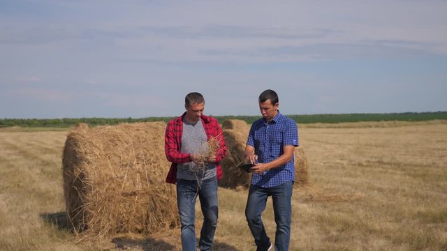 teamwork agriculture smart farming concept. two men workers farmers walking studying haystack in field on digital tablet. teamwork slow motion video. people agronomist botanist farmers working