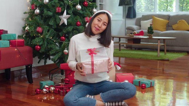 Asian women celebrate Christmas festival. Female teen wear sweater relax happy hold gift smiling near Christmas tree enjoy xmas winter holidays together in living room at home. Slow motion shot.
