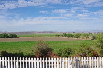 A panoramic view of the green California valley landscape along the St. Andreas fault with a white picket fence in front and blue sky