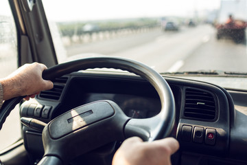 Male driver hands are holding steering wheel of truck during the movement in the road. Image with selective focus on the wheel, dashboard and blurred windshield © Zakhar Marunov