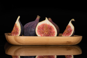 Group of two whole one half two slices of fresh fig fruit on bamboo plate isolated on black glass