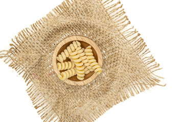 Lot of whole fresh raw pasta fusilli bucati in wooden bowl on jute cloth flatlay isolated on white background