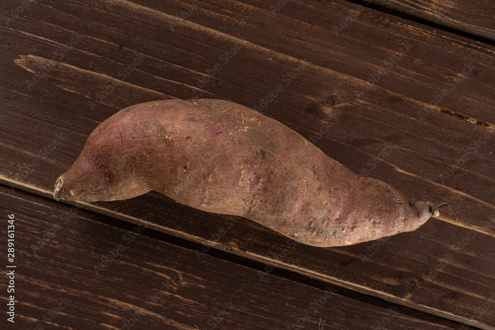 Wall mural One whole fresh brown sweet potato flatlay on brown wood