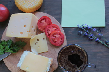 Cheese with tomatoes and coffee lies on a wooden board on a brown table