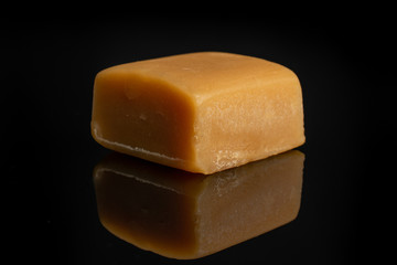 One whole sweet golden caramel candy isolated on black glass