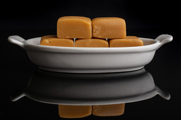 Group of five whole sweet golden caramel candy in white oval ceramic bowl isolated on black glass