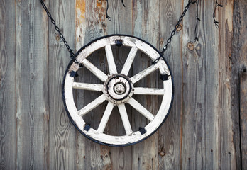 Old cart wheel hanging on vintage wooden wall.