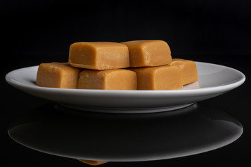 Group of six whole sweet golden caramel candy on white ceramic plate isolated on black glass