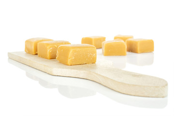 Group of seven whole sweet golden caramel candy on small wooden cutting board isolated on white background