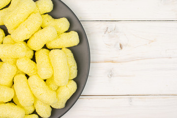 Lot of whole salted yellow corn puff on gray ceramic plate flatlay on white wood