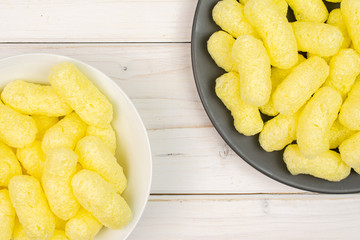 Lot of whole salted yellow corn puff on white ceramic plate on gray ceramic plate flatlay on white wood