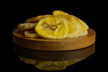 Lot of slices of sweet yellow dry banana in small group on bamboo coaster isolated on black glass