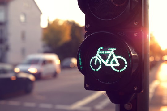 Close Up On Traffic Light For A Cycling Lane Showing Green Bicycle Symbol In Bright Toned Morning Light - Blurred Background With Cars - Urban Commuting Concept