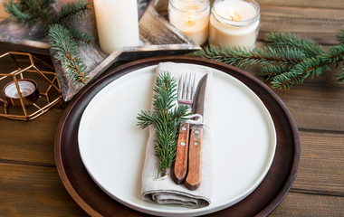 Festive Christmas table setting detail, with fr tree, wooden plate and candles on wooden table