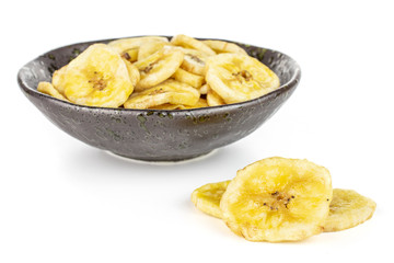 Lot of slices of sweet yellow dry banana in dark ceramic bowl isolated on white background