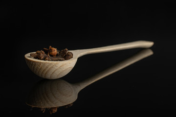 Lot of whole dry brown clove in a wooden spoon isolated on black glass