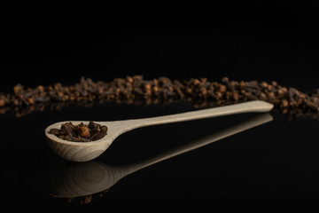 Lot of whole dry brown clove in a wooden spoon isolated on black glass