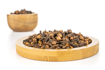 Lot of whole dry brown clove in tiny wooden bowl on bamboo coaster isolated on white background