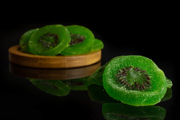 Group of four slices of sweet green candied kiwifruit on bamboo coaster isolated on black glass