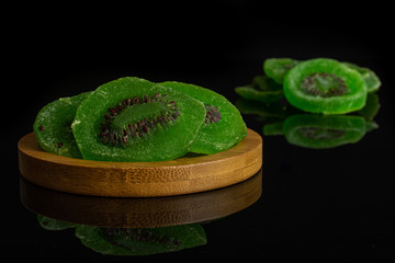 Group of seven slices of sweet green candied kiwifruit on bamboo coaster isolated on black glass