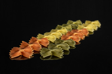 Lot of whole red, yellow and green uncooked farfalle placed diagonally isolated on black glass