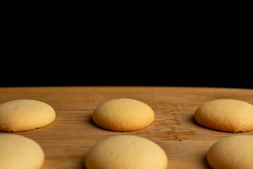 Group of six whole sweet golden sponge biscuit on bamboo cutting board isolated on black glass