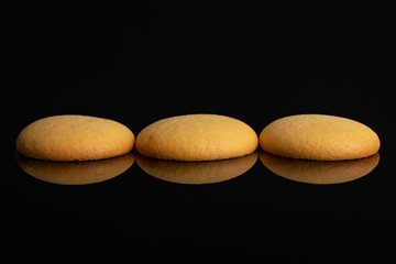 Fototapeta na wymiar Group of three whole sweet golden sponge biscuit isolated on black glass