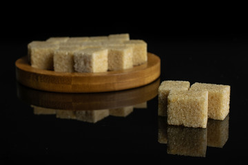 Lot of whole sweet brown sugar cube three are aside and the rest is on bamboo coaster isolated on black glass