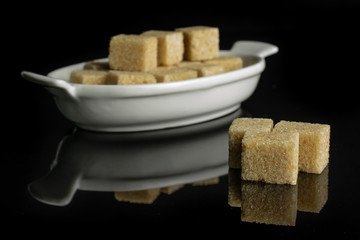 Lot of whole sweet brown sugar cube in white oval ceramic bowl isolated on black glass