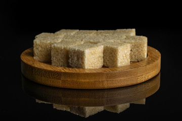 Lot of whole sweet brown sugar cube on bamboo coaster isolated on black glass