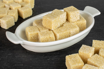 Lot of whole sweet brown sugar cube in white oval ceramic bowl on grey stone