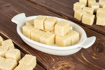 Lot of whole sweet brown sugar cube in white oval ceramic bowl on brown wood