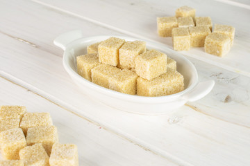 Lot of whole sweet brown sugar cube in white oval ceramic bowl on white wood