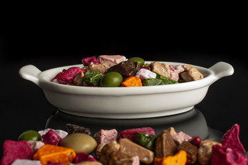 Lot of whole sweet chocolate stone in white oval ceramic bowl isolated on black glass