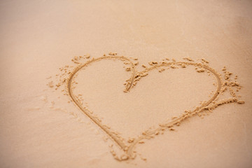Heart in the sand. Sandy heart drawing on the beach. Photo background with a symbol of love. Concept on the theme of Valentine's Day, tourism and beach holidays. Love and heart on the beach.