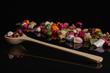 Lot of whole sweet chocolate stone in a wooden spoon isolated on black glass
