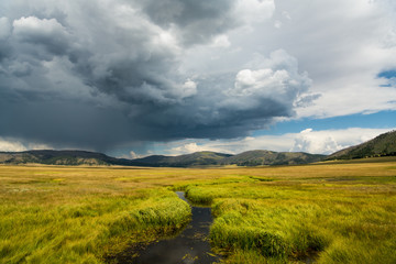 A stream winds through grasslands under a dramatic stormy sky in the Valles Caldera National...