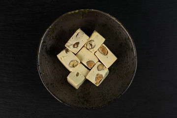 Group of seven whole sweet white nougat in dark ceramic bowl flatlay on grey stone