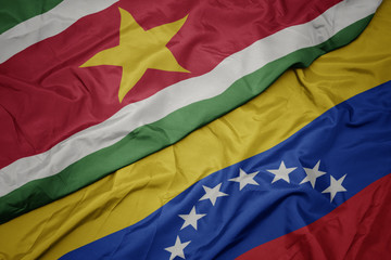 waving colorful flag of venezuela and national flag of suriname.