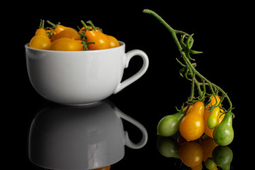 Lot of whole fresh yellow pear tomato in white ceramic cup isolated on black glass