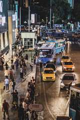 Obraz premium People who are out of work and waiting for a bus in the crowd of the city and the traffic flowing by them, buses, taxis, people, night lights of the city