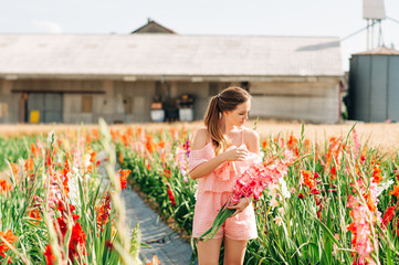 Outdoor portrait of pretty young girl in countryside, holding bouquet of gladiolus flowers - obrazy, fototapety, plakaty
