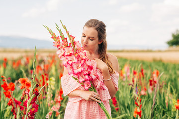 Outdoor portrait of pretty young girl in countryside, holding bouquet of gladiolus flowers